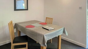 Un comedor con una mesa, sillas, un espejo enmarcado y una lámpara de pared.