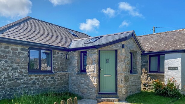 A stone house with a green door, a sloped roof, and a small garden. - Where can you experience both coast and countryside within close proximity. (Pendeen)