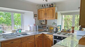A kitchen with wooden cabinets, a stove, a microwave, and a sink. - Where can you experience both coast and countryside within close proximity. (Pendeen)