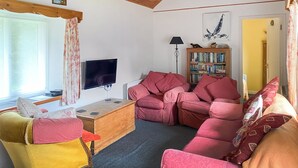 A cozy living room with a wooden ceiling, a flat-screen TV, a bookshelf, and a red sofa. - Where can you experience both coast and countryside within close proximity. (Pendeen)