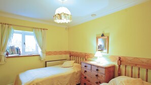 A room with two single beds, a wooden dresser, a window with curtains, and a hanging light fixture. - Where can you experience both coast and countryside within close proximity. (Pendeen)