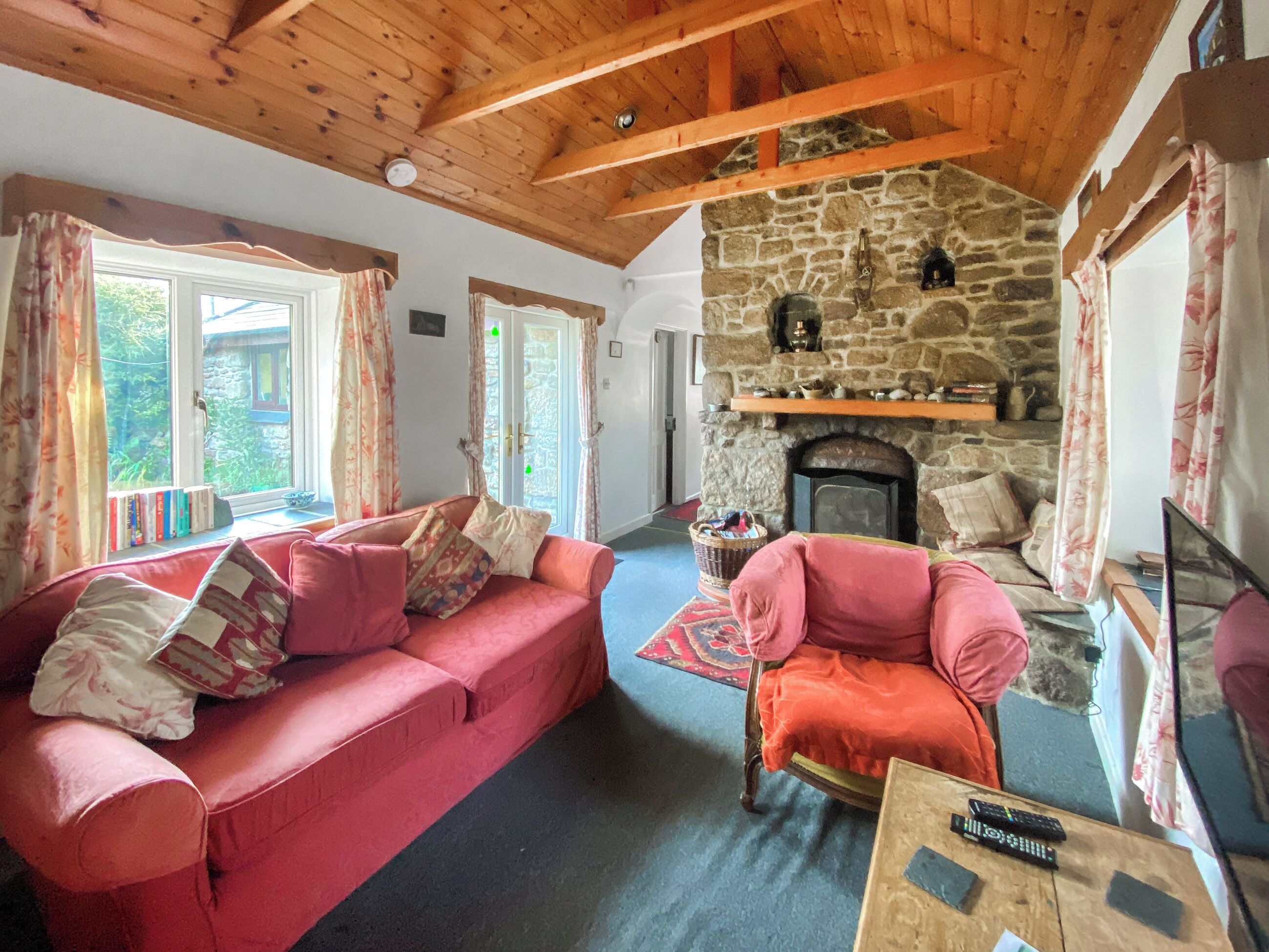 Un salon chaleureux avec une cheminée en pierre, un canapé rouge et un plafond en bois.