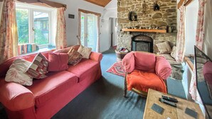 A cozy living room with a stone fireplace, a red sofa, and a wooden ceiling. - Where can you experience both coast and countryside within close proximity. (Pendeen)