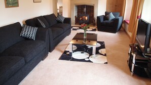 A living room with a sofa, armchair, and a TV. There is a fireplace in the background. - Gateside Farmhouse Sedbergh (Sedbergh)