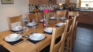 A dining table set for six with chairs, a vase with flowers, and a kitchen in the background. - Gateside Farmhouse Sedbergh (Sedbergh)