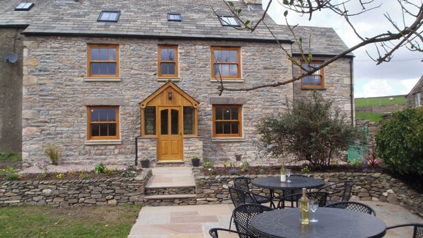 A stone house with a wooden front door, multiple windows, and a patio with outdoor seating. - Gateside Farmhouse Sedbergh (Sedbergh)
