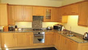 A kitchen with wooden cabinets, a granite countertop, a stove, a microwave, and a sink. - 2 bedroom accommodation in Thornthwaite (Thornthwaite)