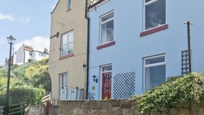 A two-story residential building with a stone wall in front, a red door, and a metal fence. - 3 bedroom accommodation in Staithes, near Whitby (Staithes, near Whitby)