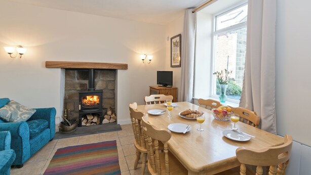 A cozy living room with a fireplace, a dining table set for two, and a comfortable blue sofa. - 3 bedroom accommodation in Staithes, near Whitby (Staithes, near Whitby)