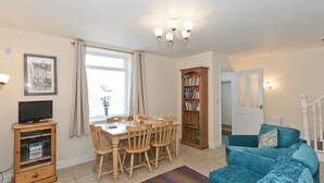 A living room with a dining table, chairs, a television, a bookshelf, and a sofa. - 3 bedroom accommodation in Staithes, near Whitby (Staithes, near Whitby)