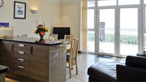 A modern kitchen with a dining area, a flat-screen TV, and a balcony with a view. - Pendine Beach Apartment (Pendine, near Amroth)