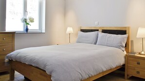 A bedroom with a bed, bedside tables, a window, and a vase with flowers. - Pendine Beach Apartment (Pendine, near Amroth)