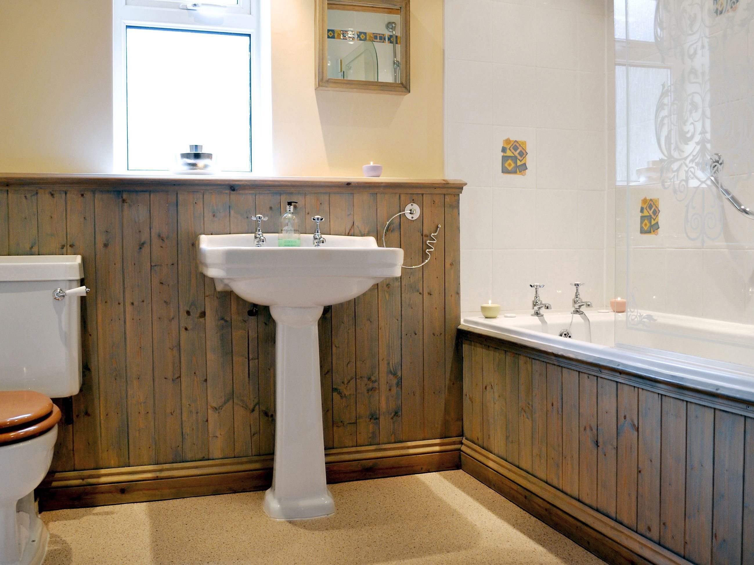Een badkamer met een wand van houten panelen, een wastafel op voetstuk, een toilet en een bad.