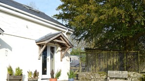 A white building with a porch, potted plants, a wooden bench, and a fenced area. - 1 bedroom accommodation in Salem, near Llandeilo (Salem, near Llandeilo)