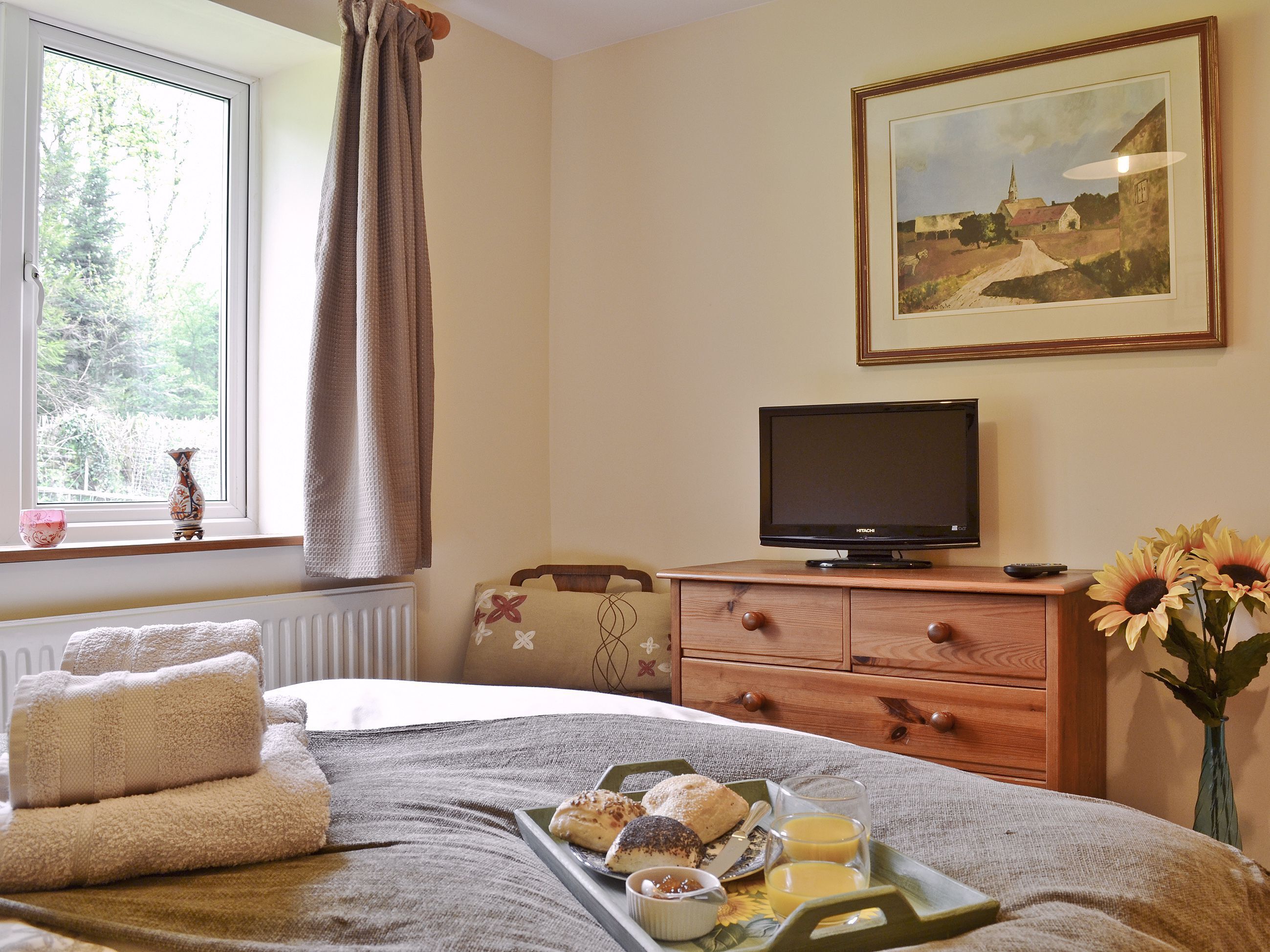 A bedroom with a bed, a dresser, a television, and a painting on the wall.