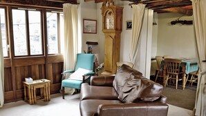 Uma sala de estar acolhedora com um sofá de couro marrom, uma poltrona verde-água, uma mesa de madeira e uma área de jantar com cadeiras de madeira.