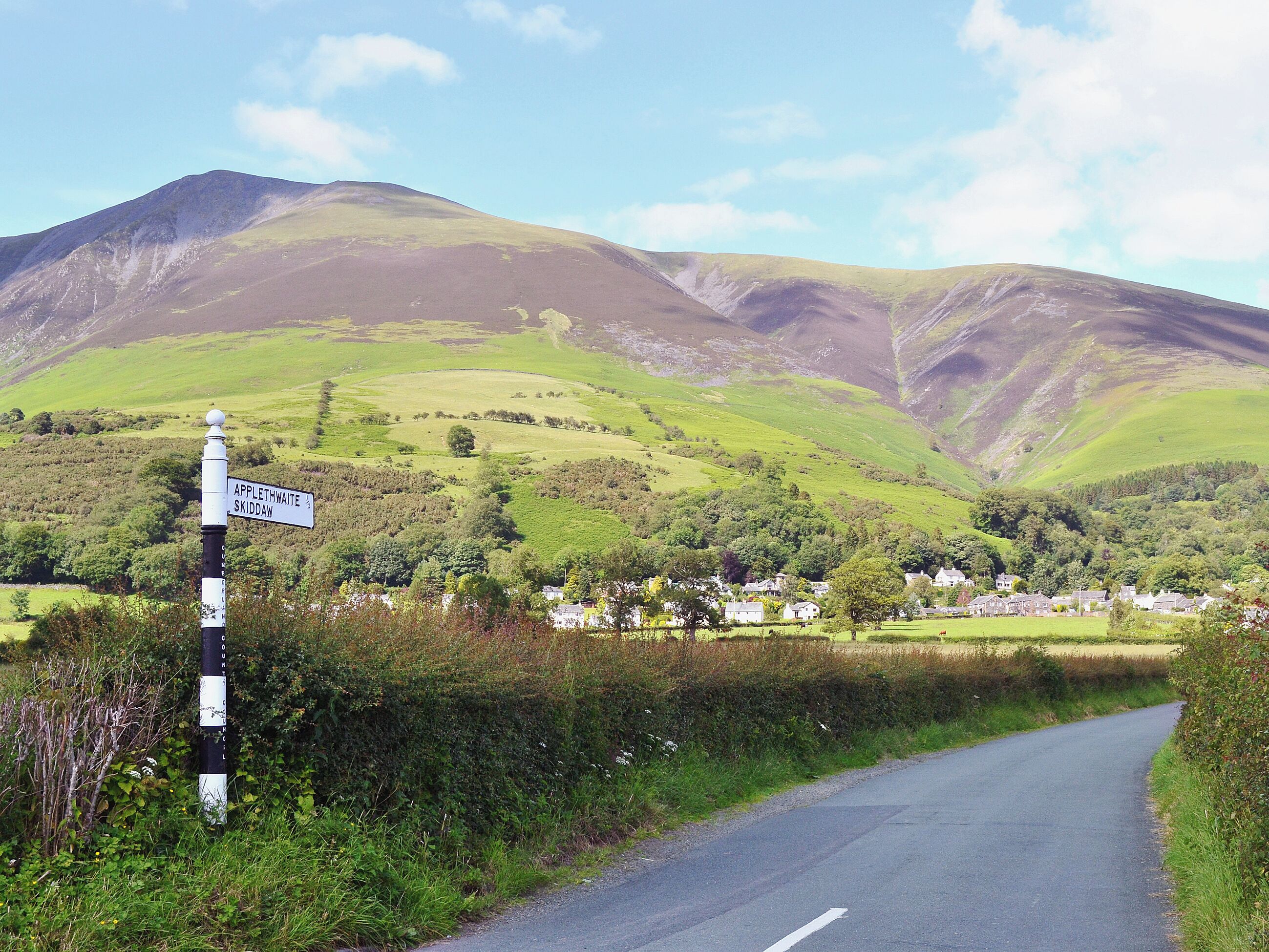 Eine ländliche Straße mit einem Wegweiser, der die Richtung nach Applethwaite und Skiddaw anzeigt.