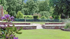 En have med et murstensbelagt stisystem, en lille dam og frodig beplantning.