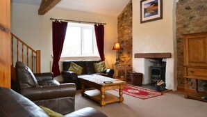 A cozy living room with a fireplace, a sofa, a coffee table, and a stone wall. - 4 bedroom accommodation in Guardhouse (Guardhouse)