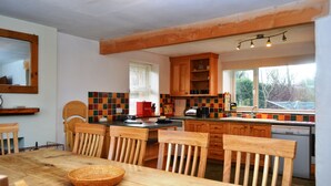 A kitchen with wooden cabinets, a dining table with chairs, and a window with a view of trees. - 4 bedroom accommodation in Guardhouse (Guardhouse)