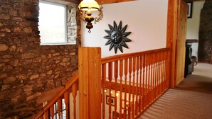 A wooden staircase with a railing, a stone wall, and a wall-mounted decorative sun. - 4 bedroom accommodation in Guardhouse (Guardhouse)