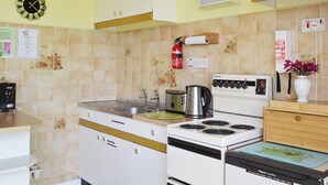 Eine Küche mit Herd, Toaster und Spüle. Ein Feuerlöscher und eine Uhr befinden sich an der Wand.