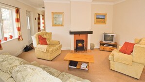 A living room with a fireplace, two armchairs, a sofa, a television, and a window with curtains. - Curlew Cottage - E3752 (Leverton)
