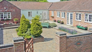 A courtyard with a brick building, a green bench, and potted plants. - Curlew Cottage - E3752 (Leverton)
