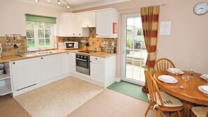 A kitchen with white cabinets, a microwave, and a dining area with a table set for two. - Curlew Cottage - E3752 (Leverton)