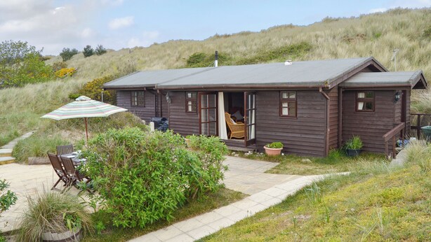 Ein Holzhaus mit Veranda, einem Esstisch mit Stühlen und einem gestreiften Sonnenschirm.