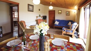Ein gemütliches Wohnzimmer mit Holzbalkendecke, einem blauen Sofa, einem Esstisch gedeckt mit Tellern und Gläsern sowie einer Vase mit Blumen.