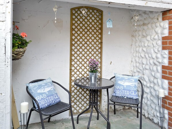 A small outdoor seating area with two chairs and a table, a decorative lattice panel, and a hanging birdhouse.