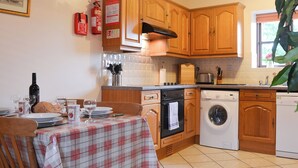 A kitchen with wooden cabinets, a table set for dining, a washing machine, and a fire extinguisher. - 2 bedroom accommodation in Caernarfon (Caernarfon)