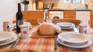 A dining table set with plates, cutlery, and a loaf of bread, with a washing machine and wooden cabinets in the background. - 2 bedroom accommodation in Caernarfon (Caernarfon)