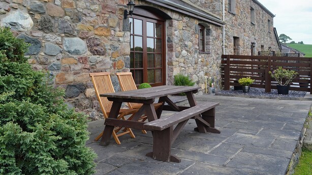 A stone building with a wooden bench and chairs outside. - 2 bedroom accommodation in Caernarfon (Caernarfon)