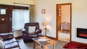 A cozy living room with a leather armchair, a wooden coffee table, and a fireplace. - 2 bedroom accommodation in Caernarfon (Caernarfon)