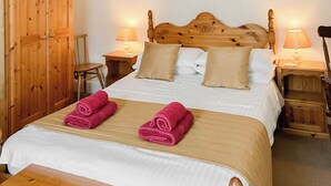 A bedroom with a wooden headboard, two bedside tables with lamps, a wooden wardrobe, and two rolled towels on the bed. - Atlantic House - 27665 (Port Isaac)