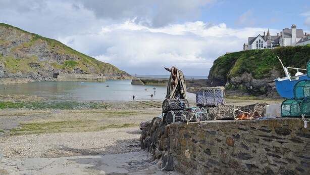 A coastal scene with a rocky shoreline, fishing gear, and a building on a cliff. - Atlantic House - 27665 (Port Isaac)