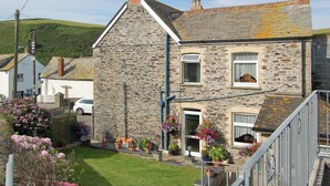 A stone house with a steep gabled roof, a front porch with hanging flower baskets, and a visible number '43' on the door. - Atlantic House - 27665 (Port Isaac)