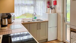 A modern kitchen with a sink, stove, and refrigerator. There is a window with a view of greenery outside. - Atlantic House - 27665 (Port Isaac)