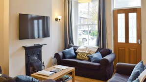 A living room with a sofa, a coffee table, a TV, a fireplace, and a window with curtains. - 4 bedroom accommodation in Keswick (Keswick)