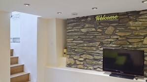 A staircase leading to a landing with a stone wall and a 'Welcome' sign above a flat-screen TV. - 4 bedroom accommodation in Keswick (Keswick)