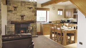 A cozy living room with a stone fireplace, a dining area with wooden furniture, and a kitchen with wooden cabinets and a microwave.