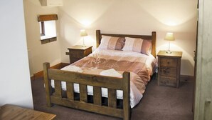A bedroom with a wooden bed, two bedside tables with lamps, a window with a view, and a radiator.
