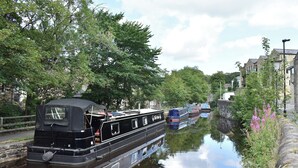 A narrow canal with boats docked along the sides, surrounded by trees and buildings.