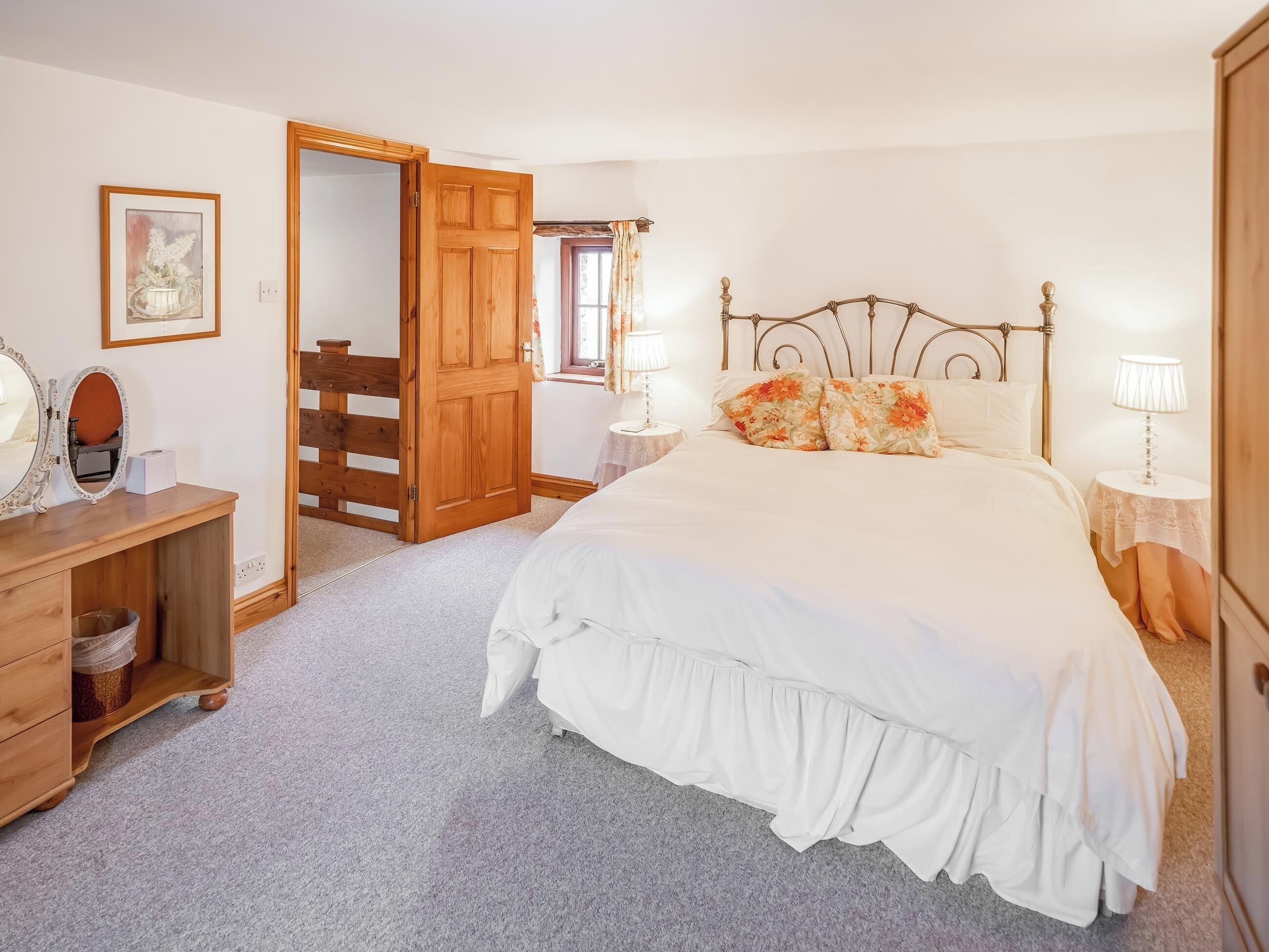A bedroom with a bed, bedside tables, a dresser, a mirror, a door, and a window with curtains.