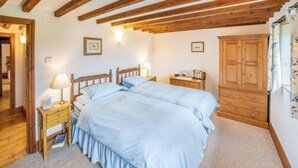 Une chambre avec deux lits, des têtes de lit en bois, une table de chevet avec une lampe, une commode et une armoire.