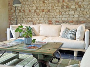 A cozy living area with a stone wall, a white sofa, striped pillows, a blue vase with a plant, and a wooden coffee table with magazines.