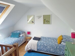 Ein Schlafzimmer mit zwei Betten, einem Holzstuhl, einem kleinen Tisch und einer grünen Kommode.