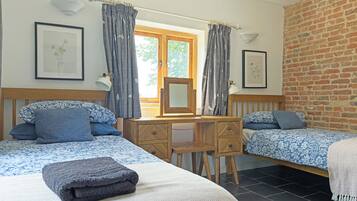 A bedroom with two beds, a wooden desk, a chair, a mirror, and a window with curtains.